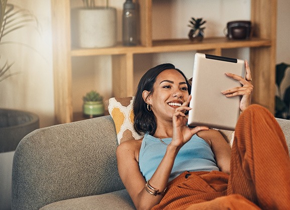 Smiling woman looking at tablet while relaxing on couch
