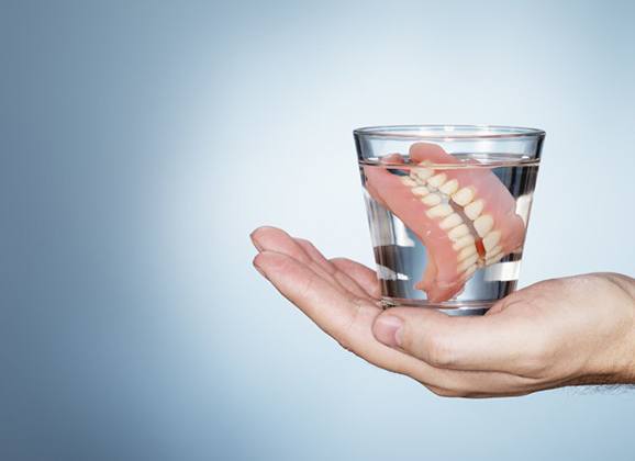 hand holding full denture in glass of water 